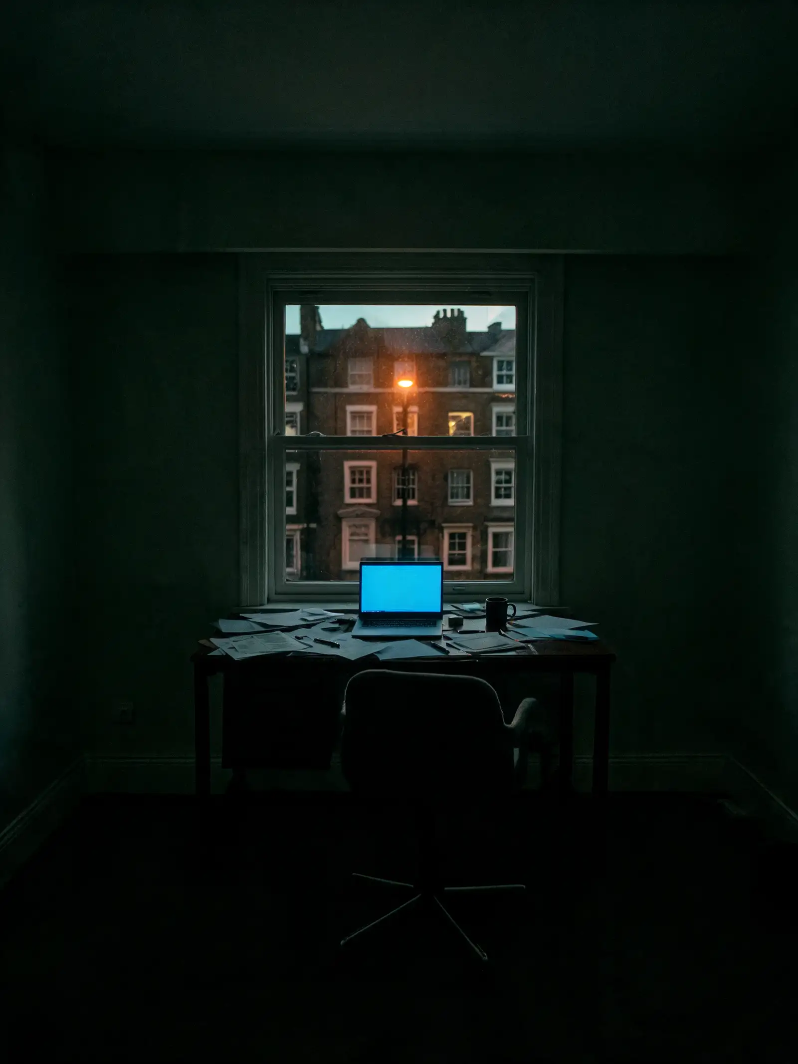 A dark home office at night, laptop still glowing
